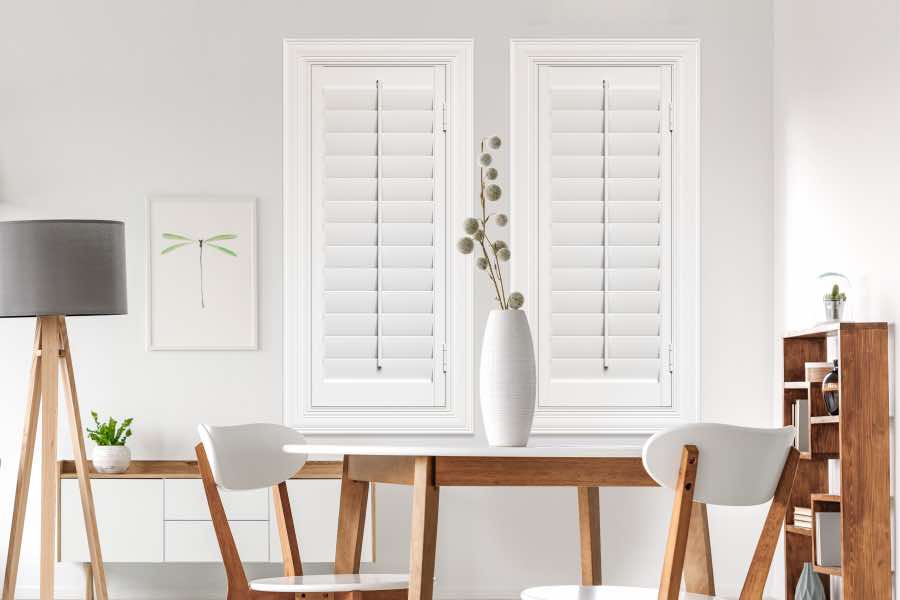 White Polywood plantation shutters on two skinny windows in a white dining room